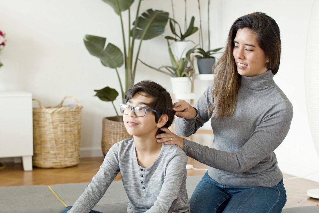 A mother lovingly combs her son's hair, creating a warm family moment indoors.