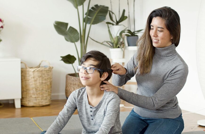 A mother lovingly combs her son's hair, creating a warm family moment indoors.