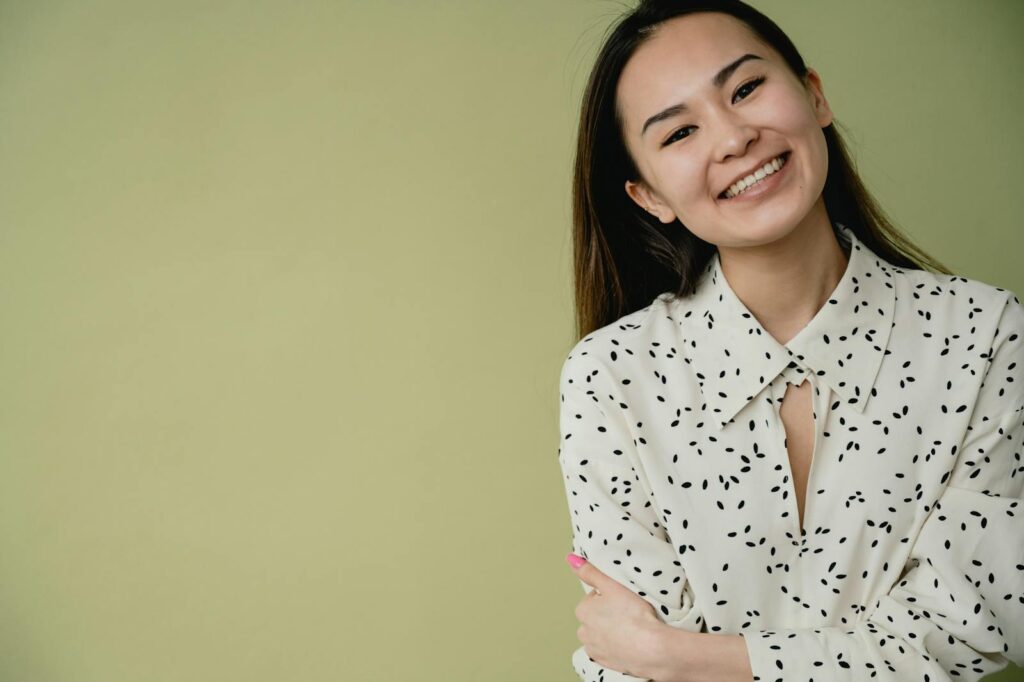 Cheerful woman in white patterned dress smiling at the camera on a green backdrop.