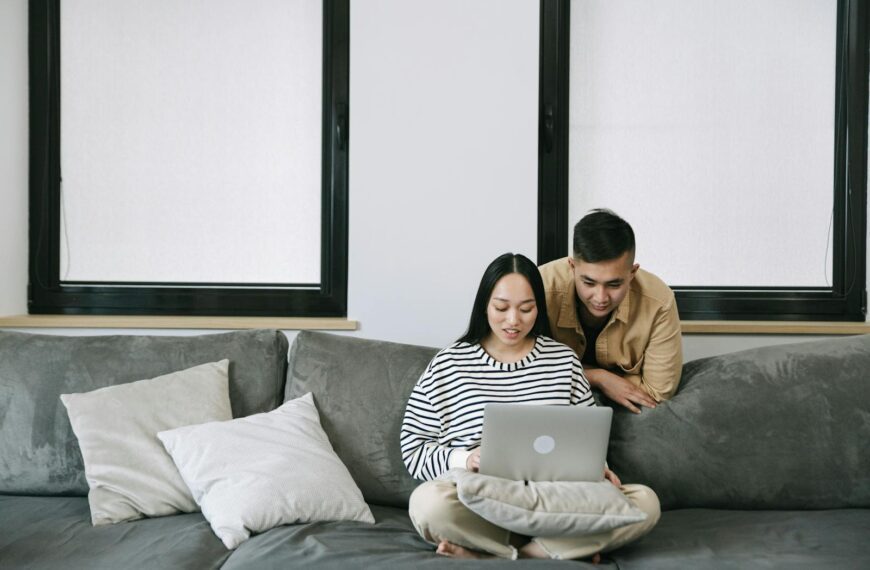 A couple enjoying a cozy moment indoors while using a laptop on the sofa.