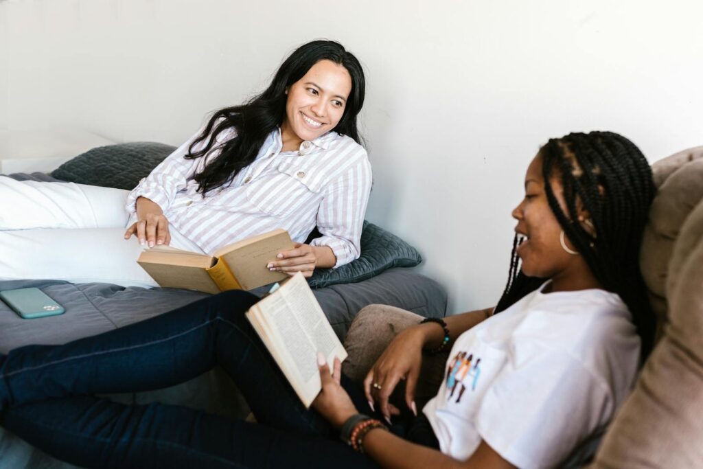 Two women enjoy reading books and studying together in a cozy indoor setting.