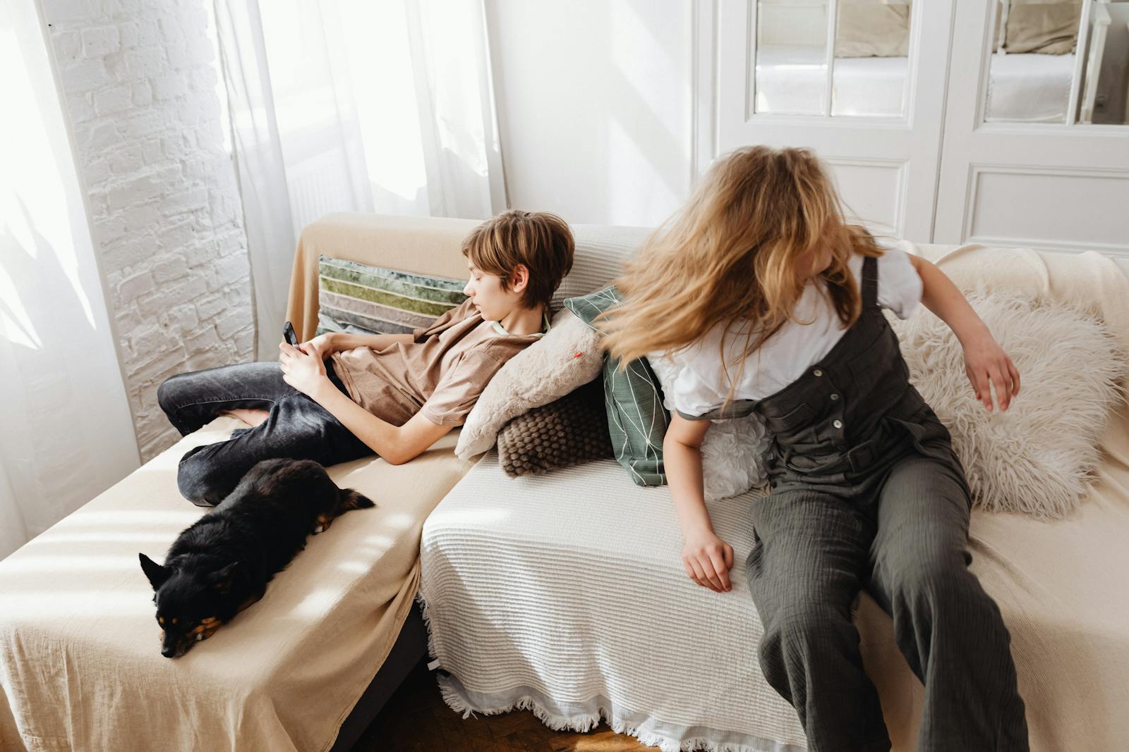 A boy and girl relaxing with their dog on a comfortable living room sofa, enjoying warmth and togetherness.