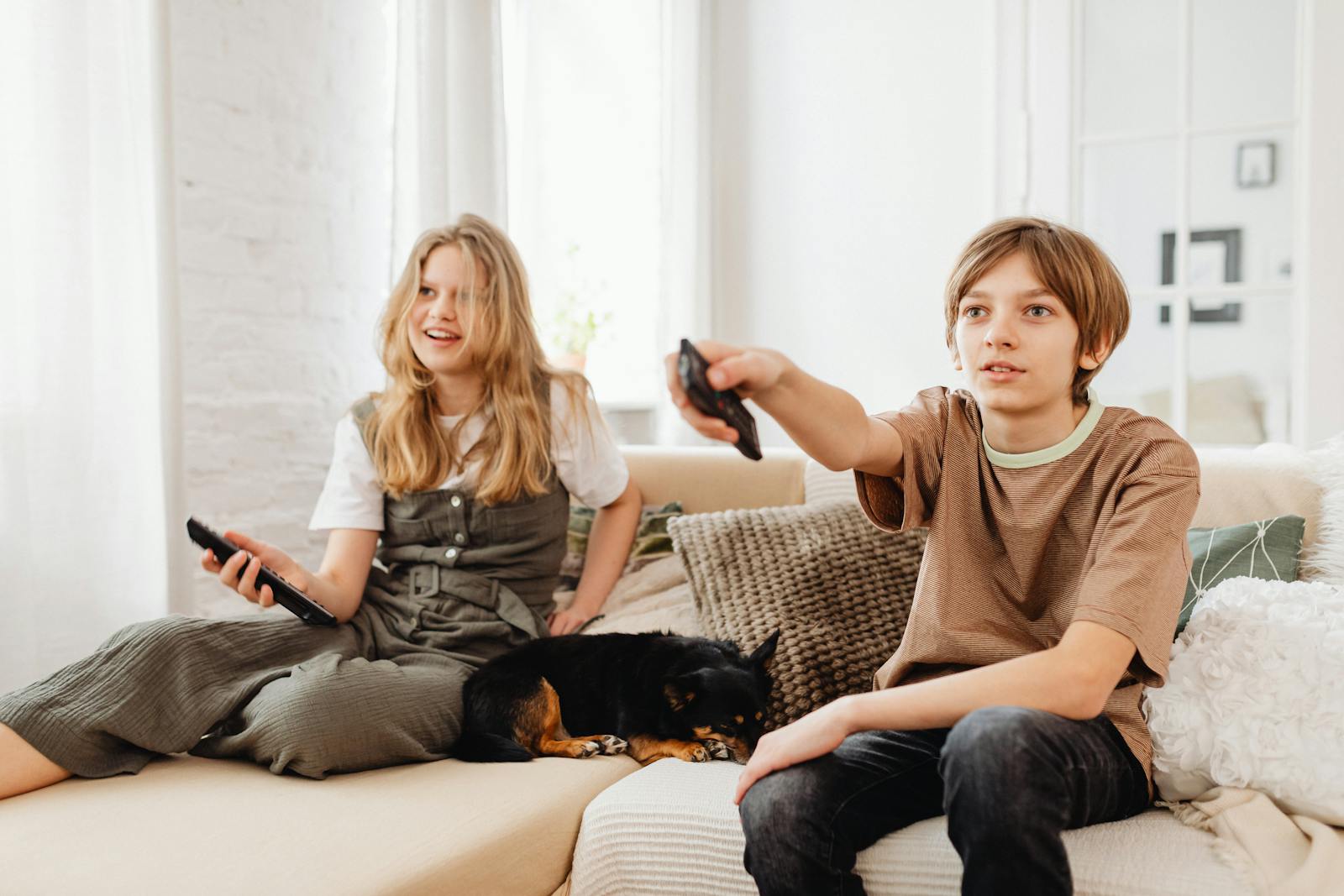 Two kids sitting on a couch with their pet dog, watching TV indoors.
