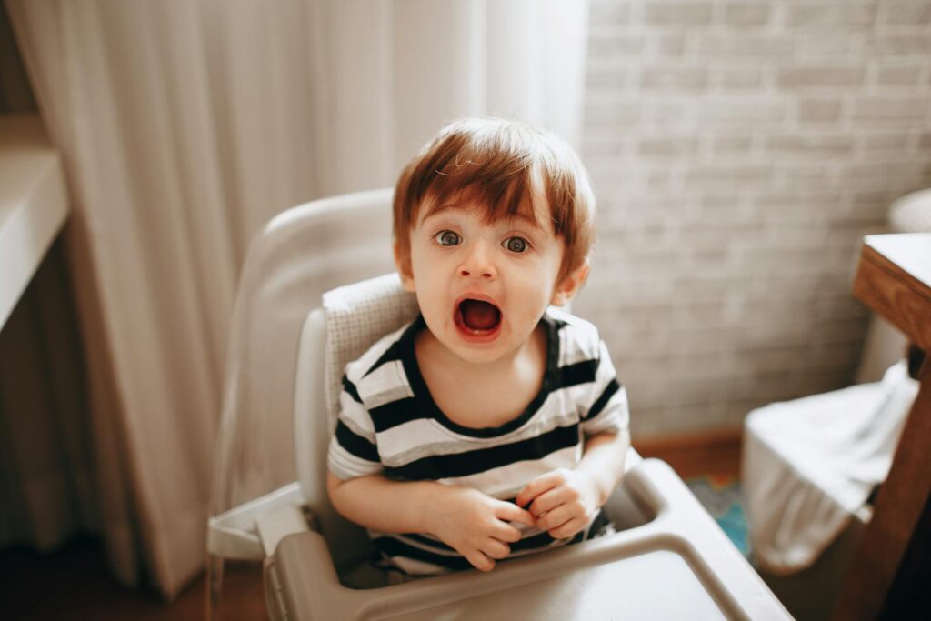 Close-up of a cheerful toddler in a high chair, playfully engaged indoors.