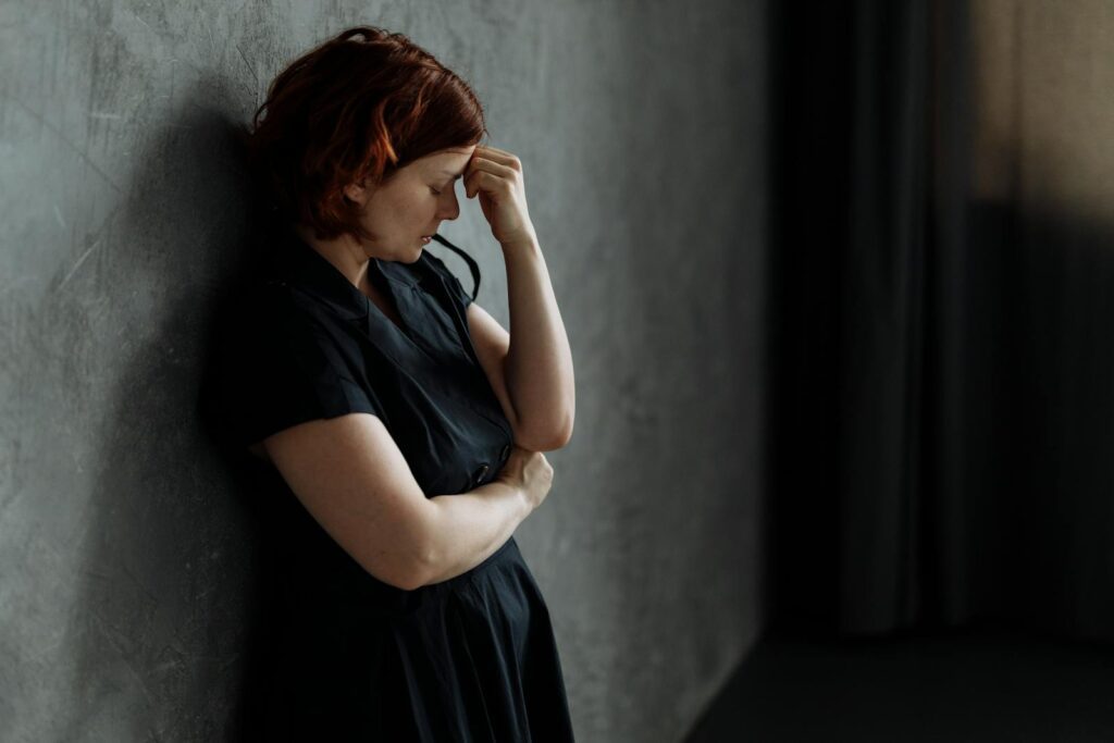 A woman in stress leaning against a concrete wall with eyes closed, conveying deep emotion.