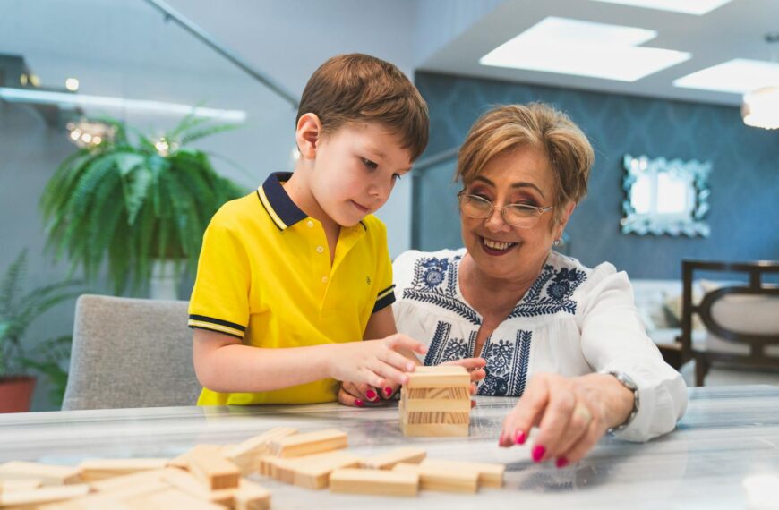 A cheerful grandmother and her grandson play Jenga together indoors, enjoying quality time.