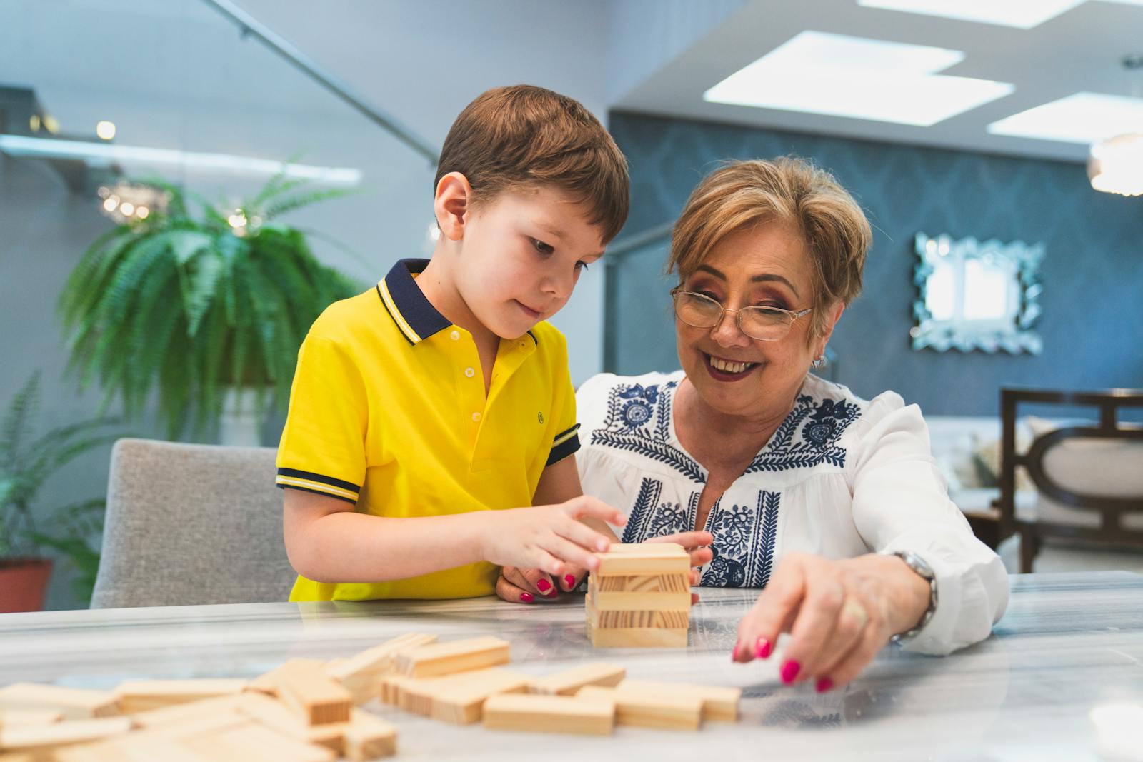 A cheerful grandmother and her grandson play Jenga together indoors, enjoying quality time.