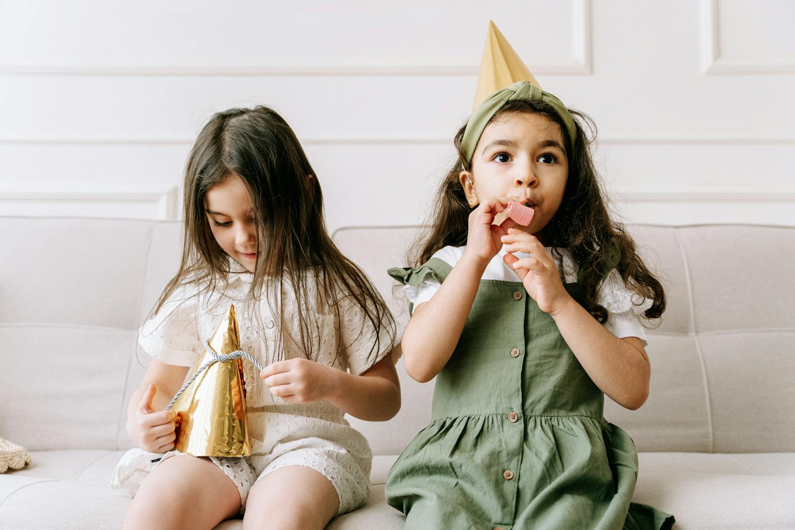 Two young girls in party hats enjoying a birthday celebration indoors.