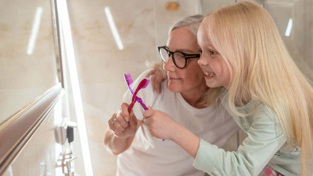 A joyful moment of oral hygiene with a grandmother and granddaughter in the bathroom.