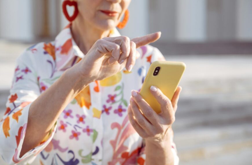 Elegant senior woman in floral blouse using a smartphone outdoors.