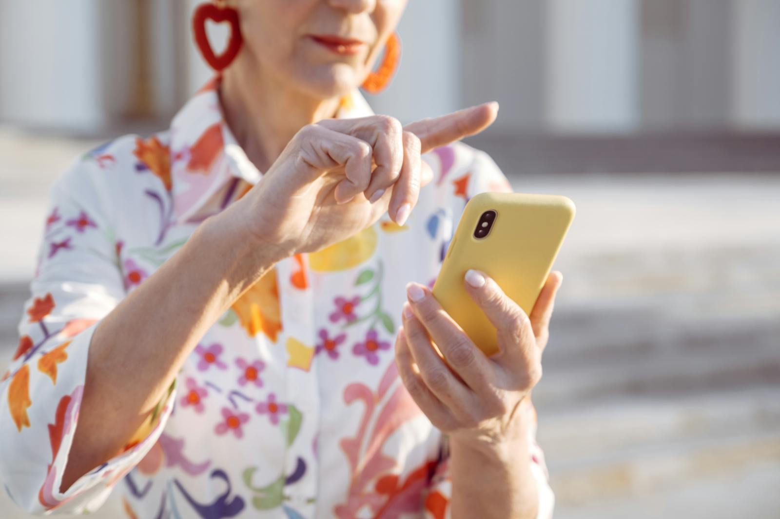 Elegant senior woman in floral blouse using a smartphone outdoors.