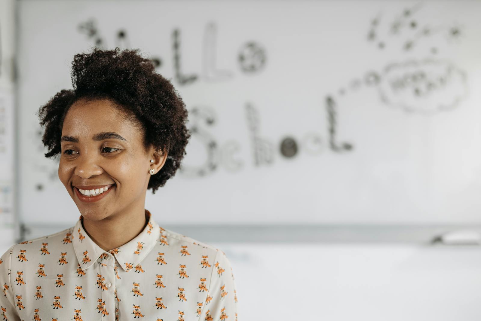 A friendly female teacher smiles in front of a classroom whiteboard.