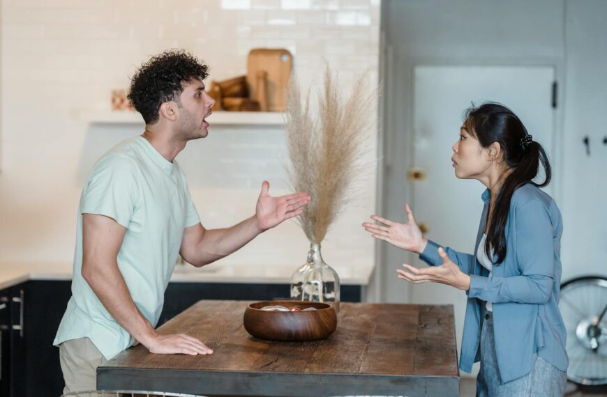 A couple engages in a heated argument at a wooden table in a modern indoor setting.
