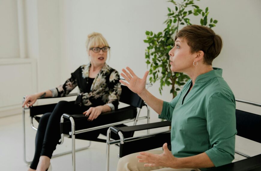 Two women engaged in a serious discussion in a modern office setting, highlighting communication and mental health.