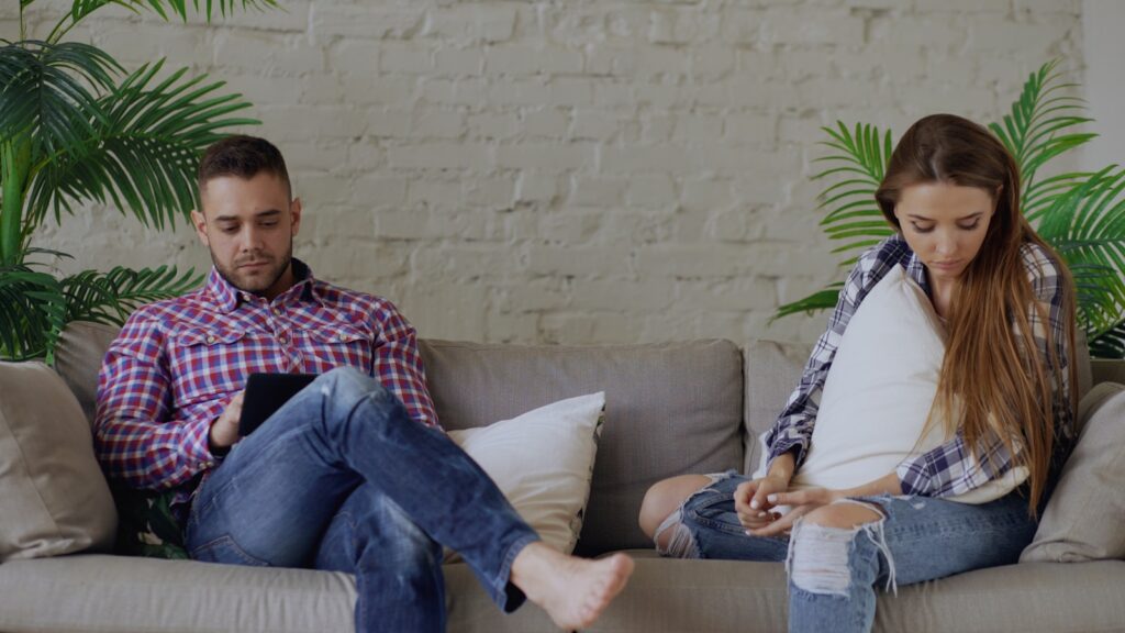 Couple sitting on sofa looking at phones