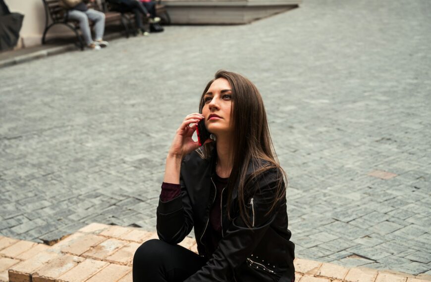woman in black leather jacket sitting on brown brick floor during daytime
