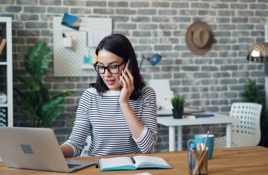 a woman talking on a cell phone while using a laptop