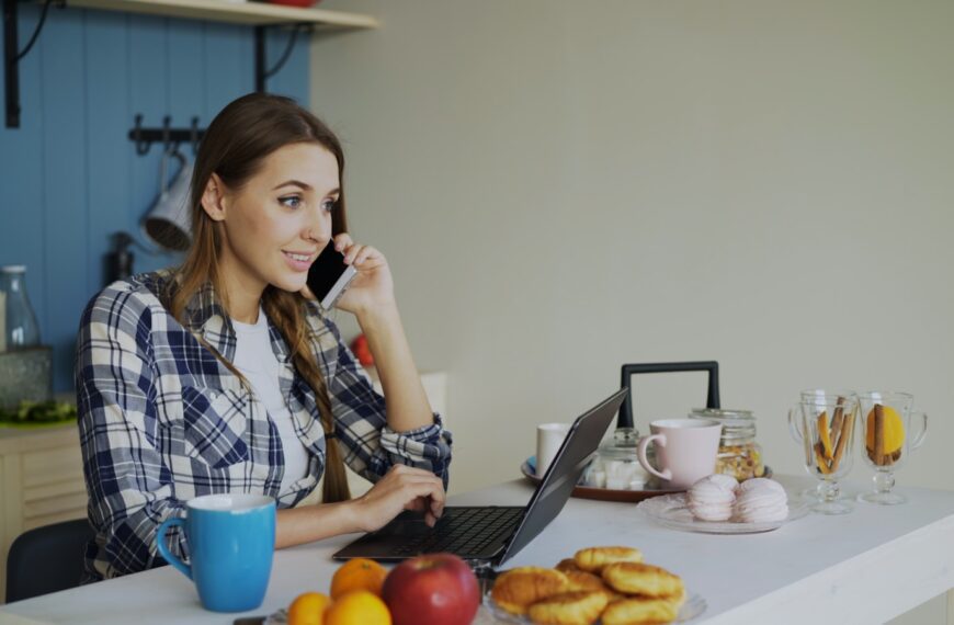 Woman talking on phone while working on laptop at table.