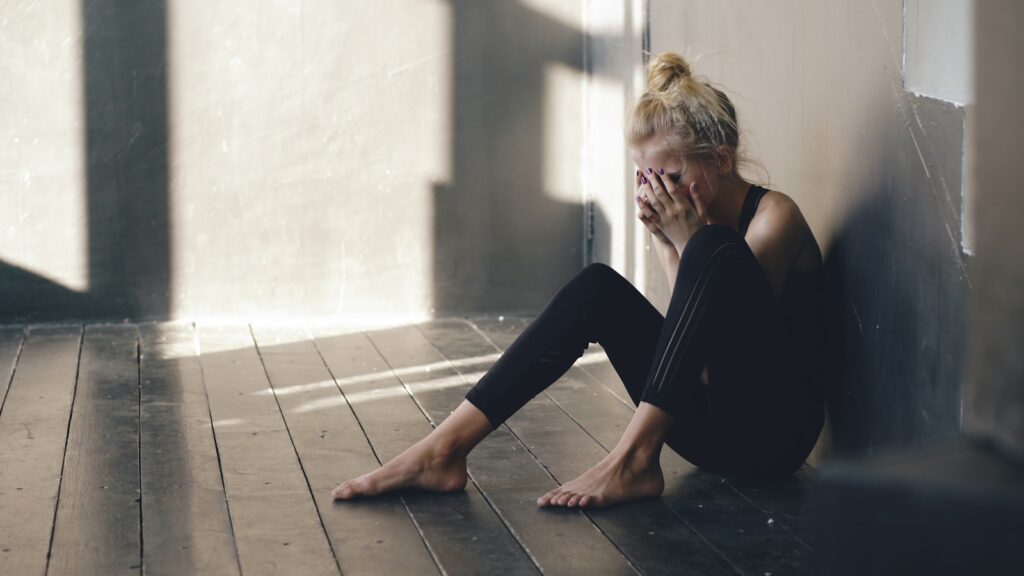 Woman sitting on floor, covering face with hands.