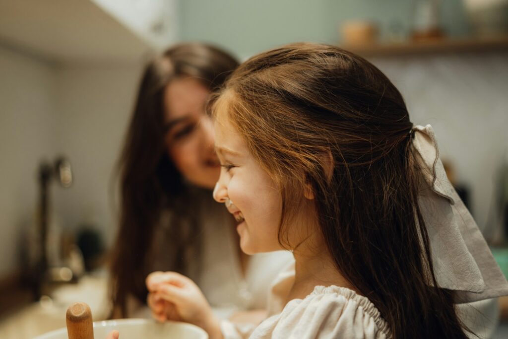 A little girl sitting in front of a sink next to a woman