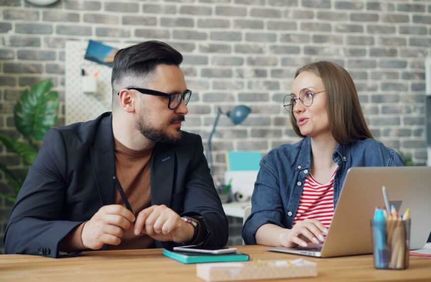 a man and a woman sitting at a table looking at a laptop