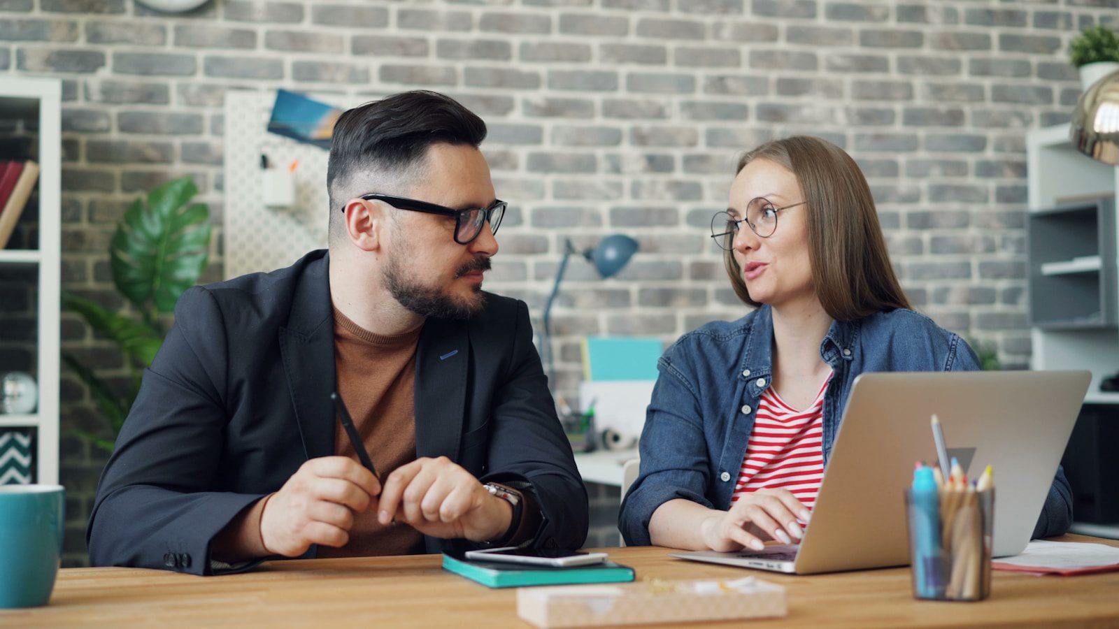 a man and a woman sitting at a table looking at a laptop
