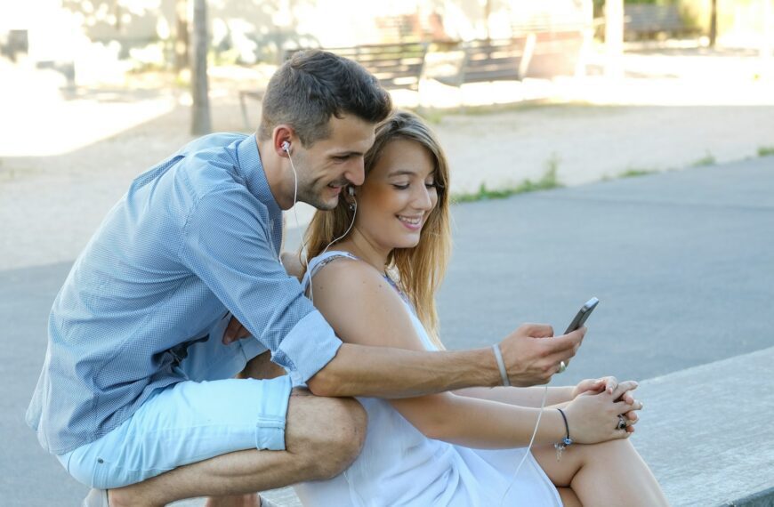 a man and a woman sitting on a bench looking at a cell phone