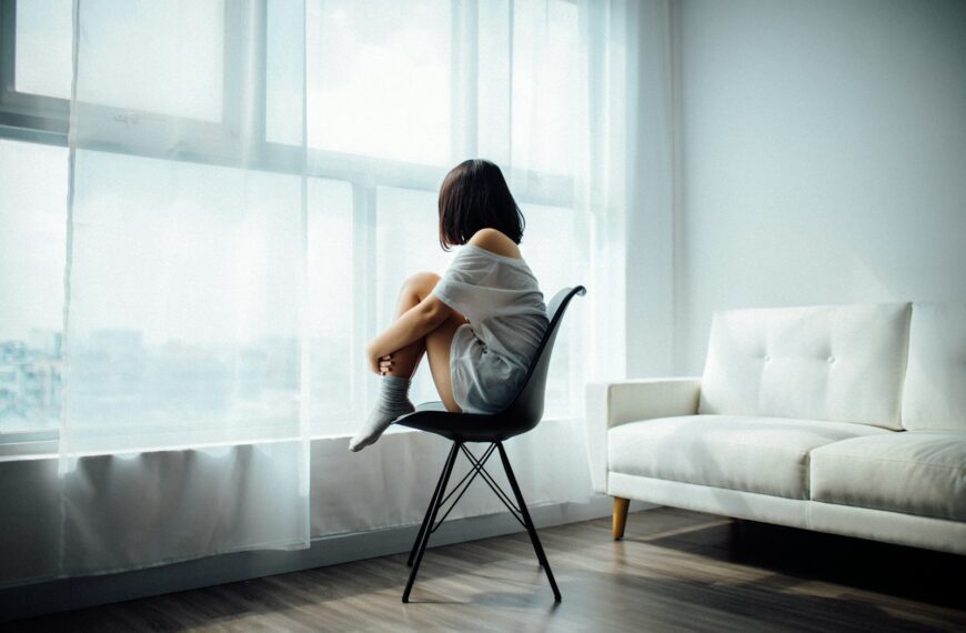woman sitting on black chair in front of glass-panel window with white curtains