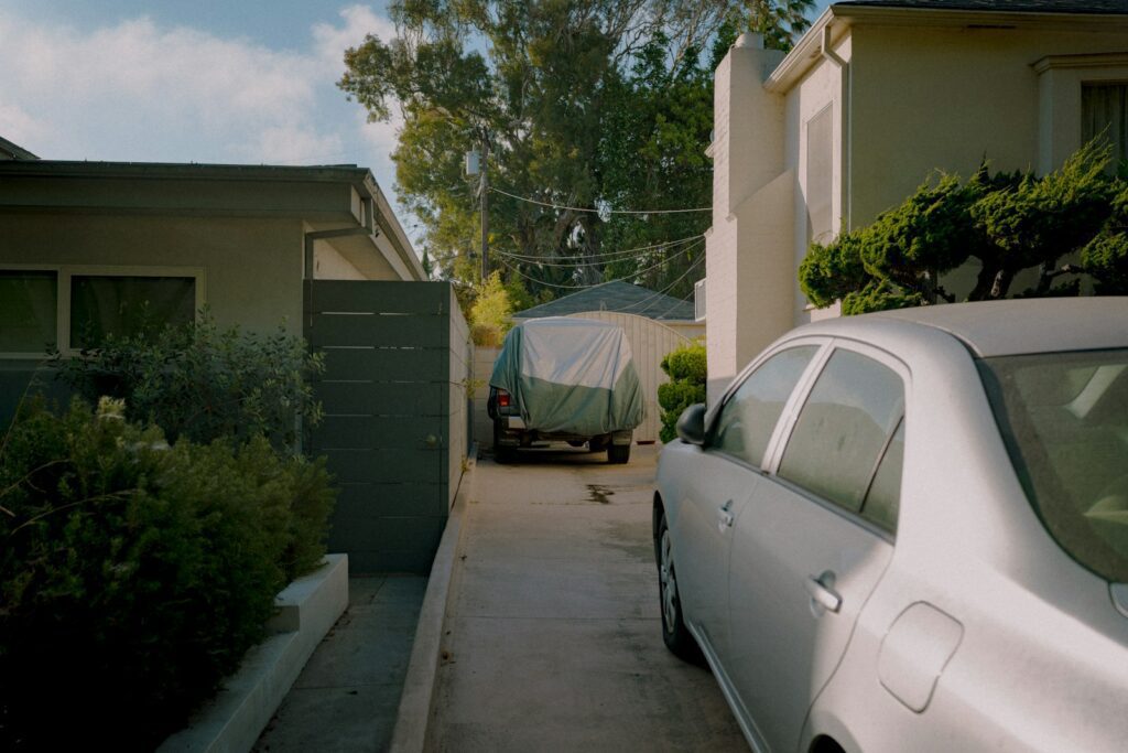 A car parked in a narrow driveway between houses.