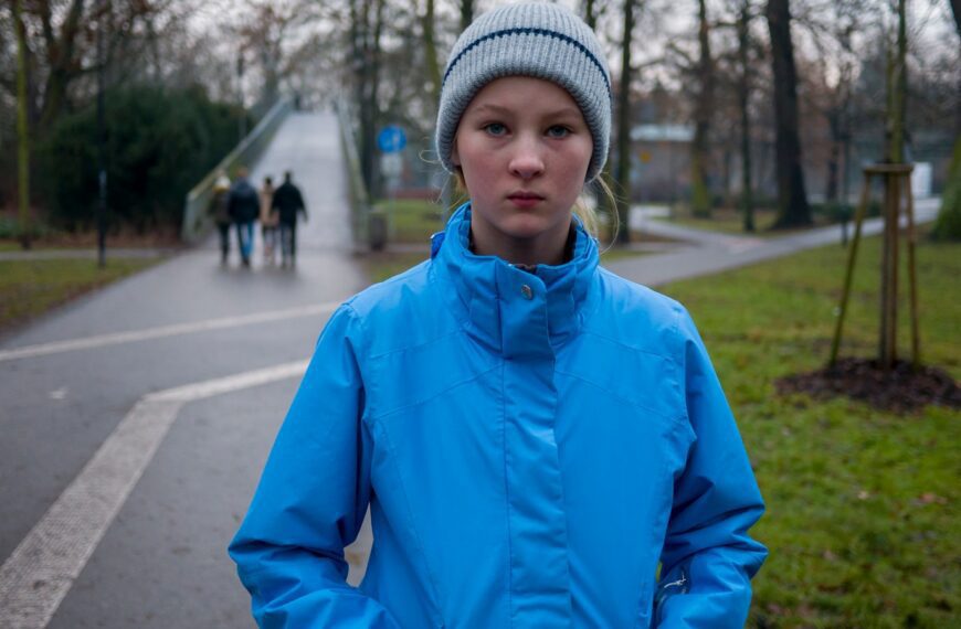 boy in blue jacket and gray knit cap standing on sidewalk during daytime