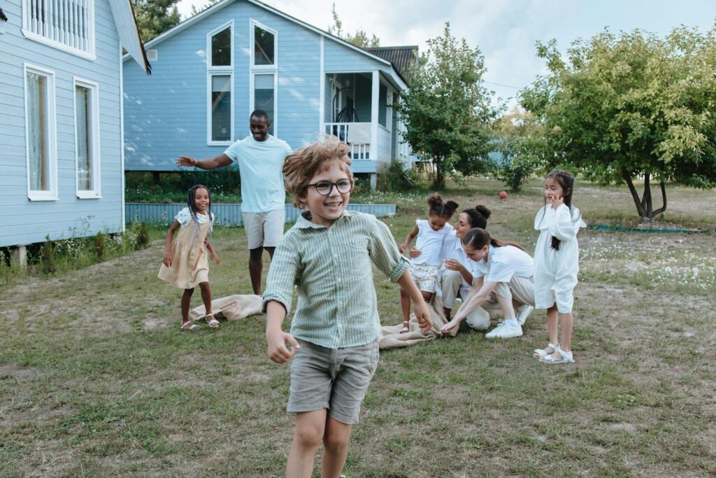 Children and adults enjoy a playful time outdoors near blue houses.
