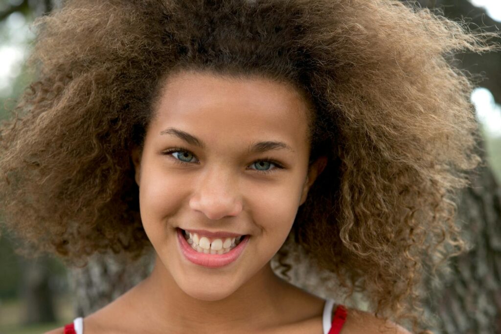 A smiling teenager with beautiful natural curls enjoying the day outdoors, embodying vibrant youthfulness.