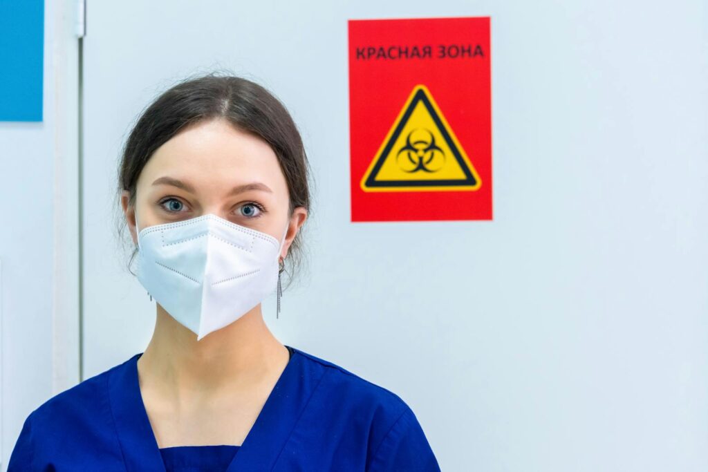 Healthcare professional in protective gear standing near a biohazard warning sign.