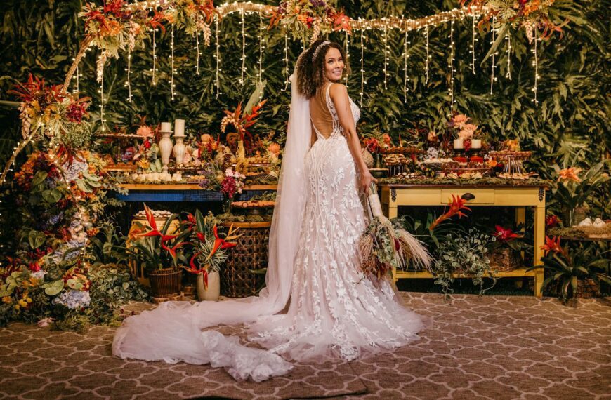 A joyful bride in a floral wedding dress amidst lush tropical decor and vivid floral arrangements.