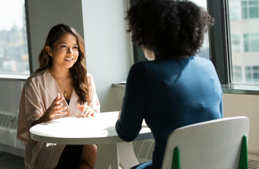 Two women sitting at a table having a professional discussion in a bright office setting.