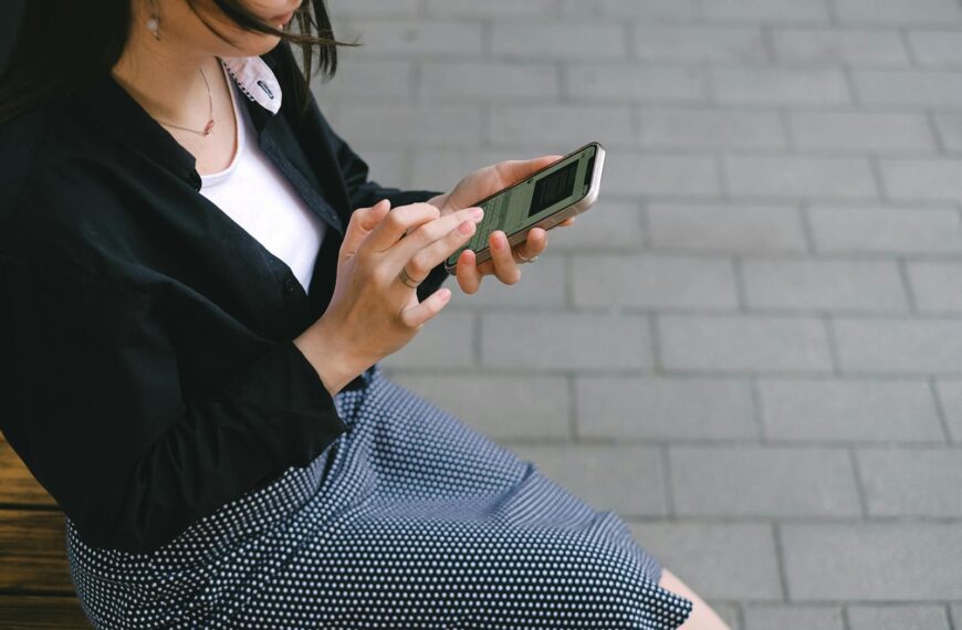 A woman using a smartphone outdoors in an urban setting, wearing a polka-dotted dress.