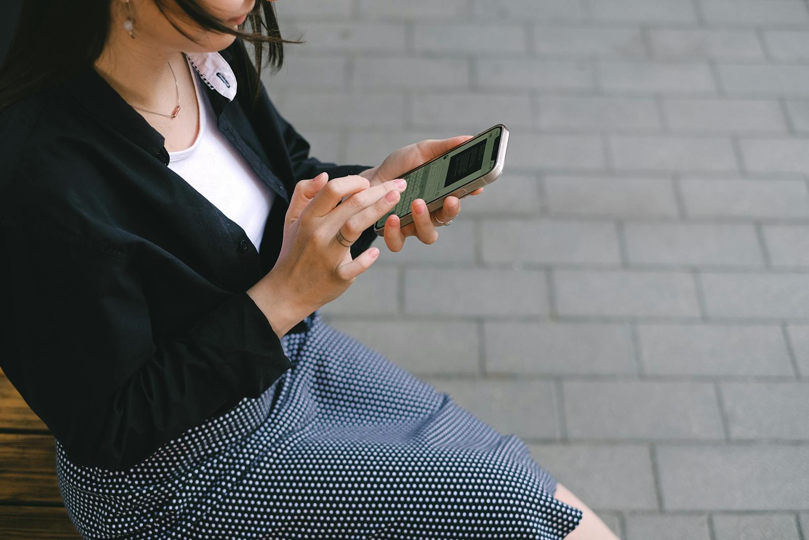A woman using a smartphone outdoors in an urban setting, wearing a polka-dotted dress.