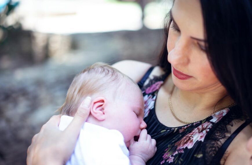 Tender moment of a mother holding her sleeping newborn baby outdoors.