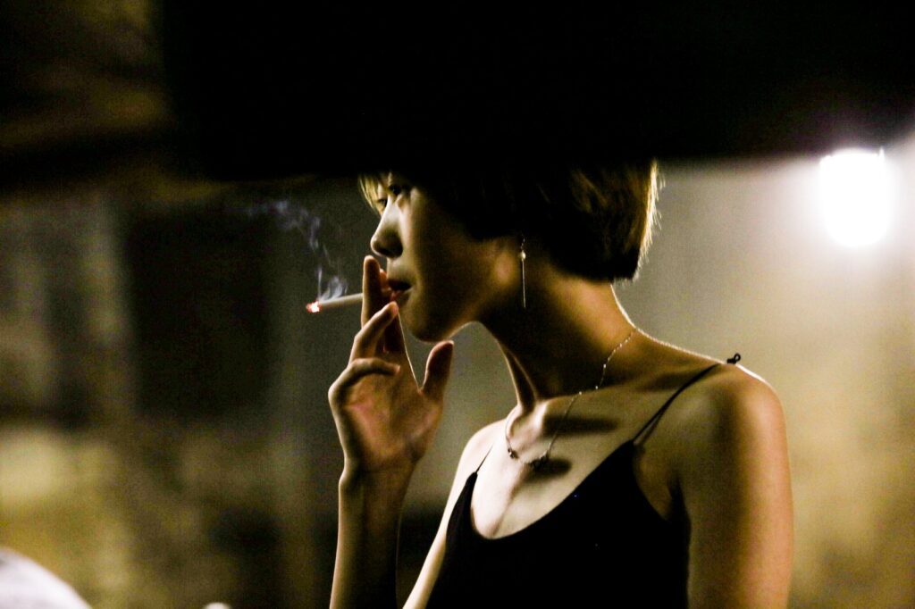 Portrait of a young woman smoking a cigarette outdoors at night in an urban setting.