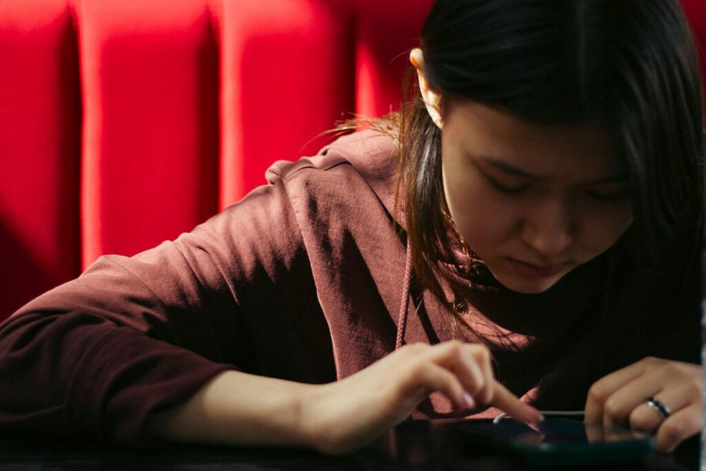 Young woman focused on her smartphone with a bright red background, representing modern technology lifestyle.