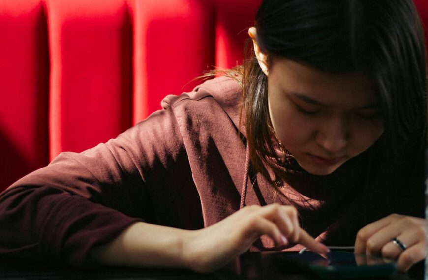 Young woman focused on her smartphone with a bright red background, representing modern technology lifestyle.