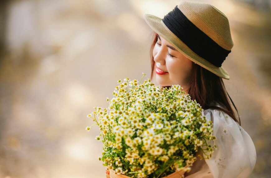 A woman in a straw hat enjoying a bouquet of daisies on a sunny day.