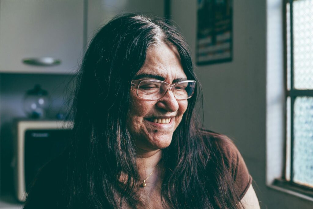 Elderly woman with glasses smiling in a kitchen setting.