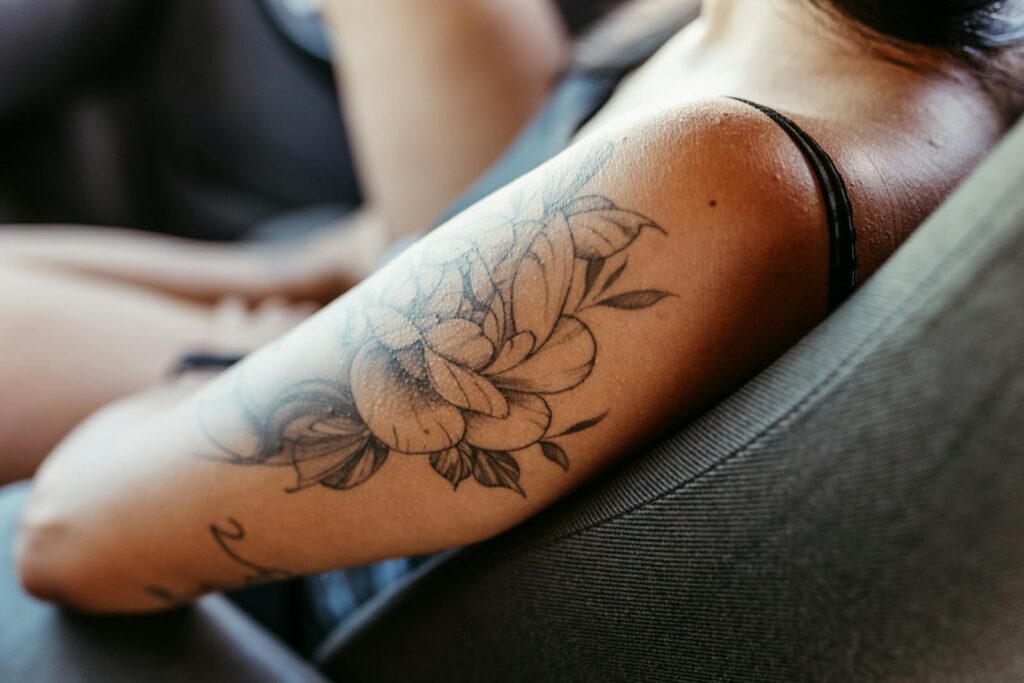 Close-up of a woman's arm with a detailed floral tattoo while she sits relaxed in a chair.