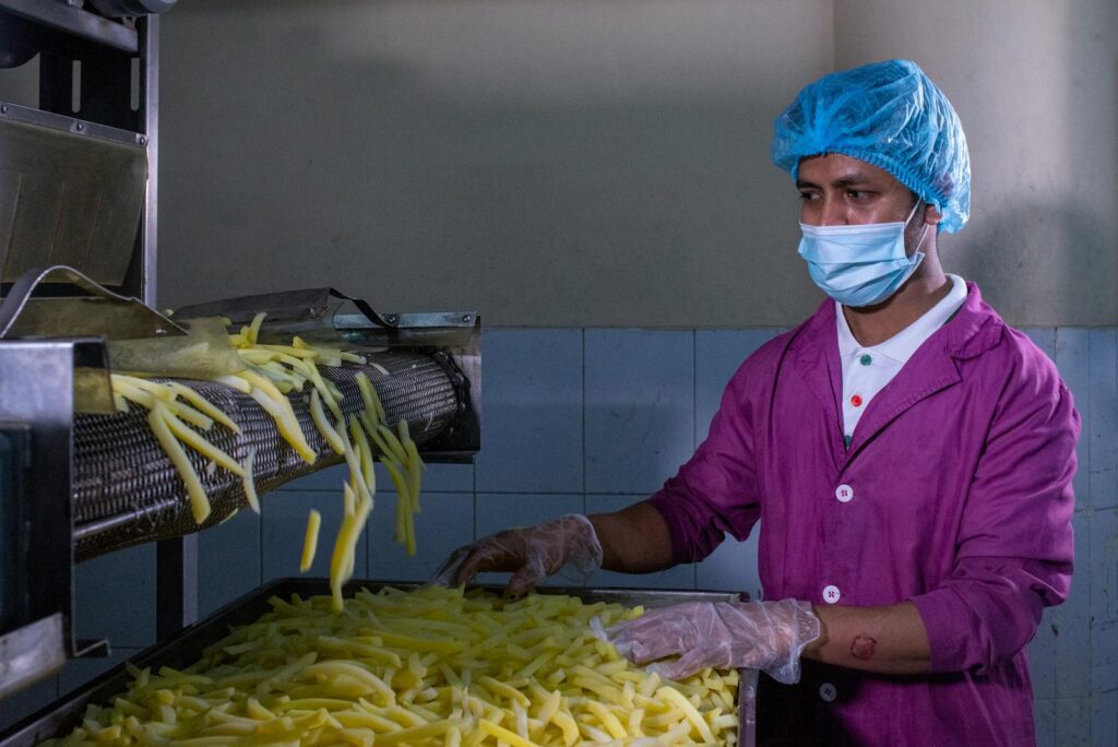 A factory worker in protective gear monitors the production of French fries, ensuring quality control.