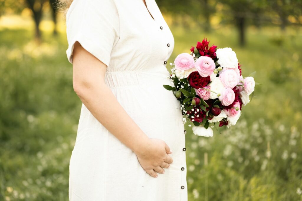 Pregnant woman holds flowers.
