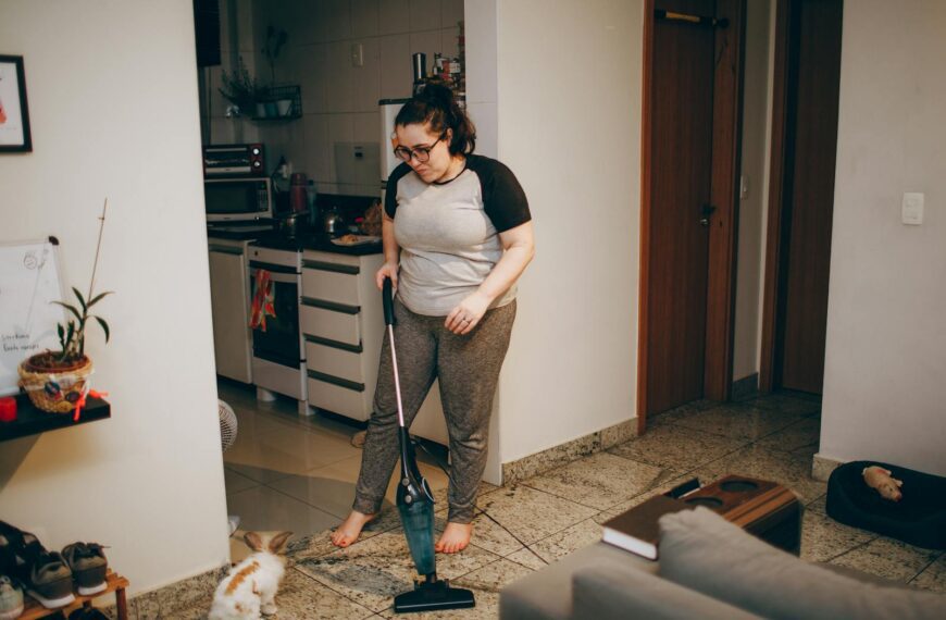 A woman cleaning her living room with a vacuum cleaner while her pet rabbit watches.