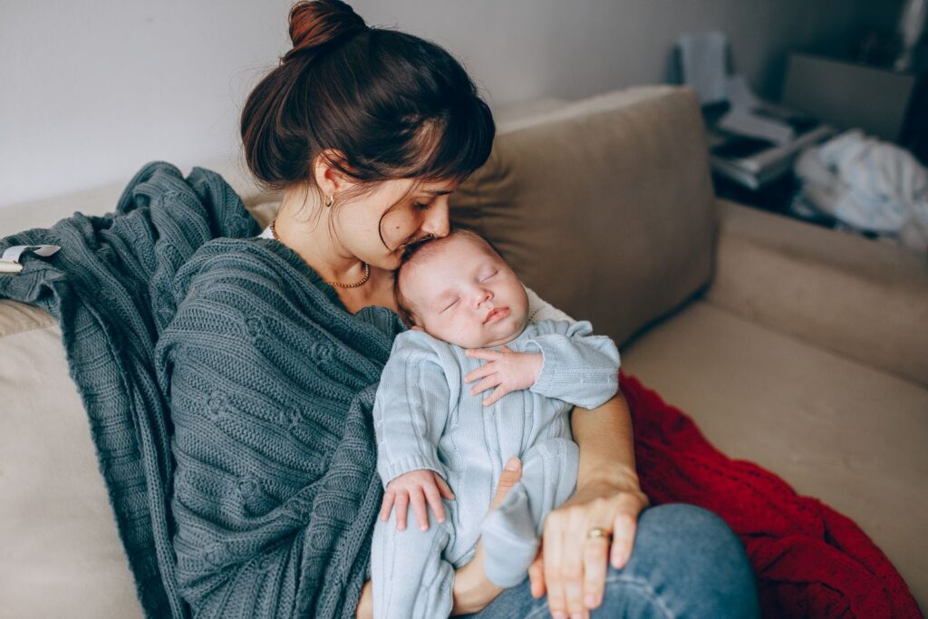 A mother lovingly holds her sleeping baby on a cozy sofa, wrapped in warmth and affection.