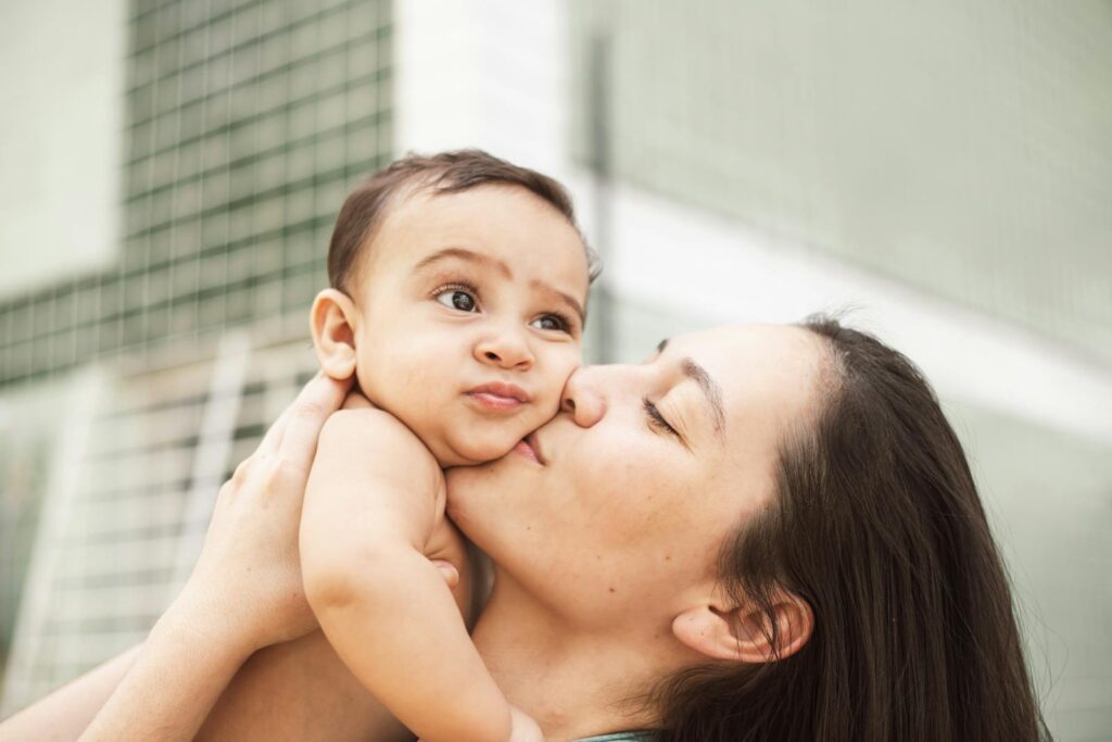 A loving mother kisses her baby, capturing a sweet moment of affection and intimacy indoors.
