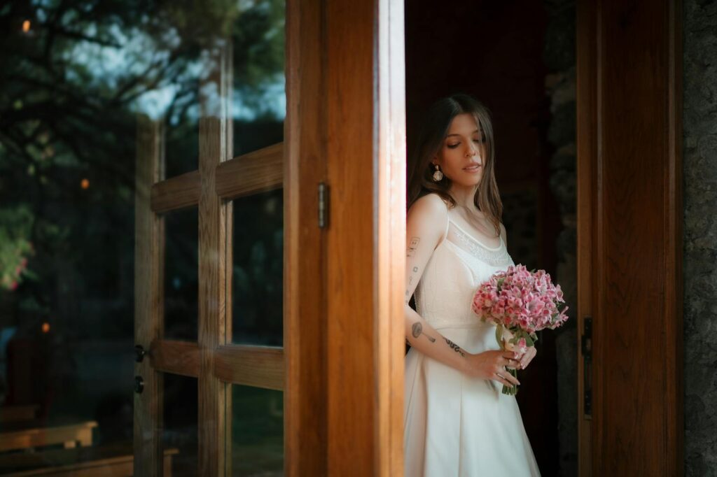 Elegant bride in white dress holding bouquet near rustic wooden door in Santiago de Querétaro.